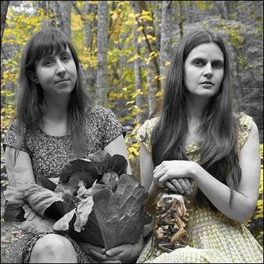 A couple of women sitting in a forest

Description automatically generated