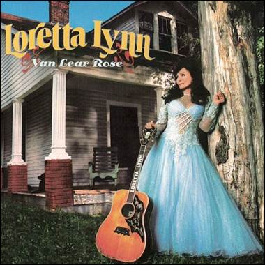 A person in a blue dress leaning against a tree with a guitar

Description automatically generated