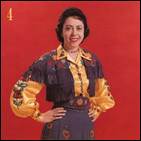 The image depicts a woman wearing a colorful, floral dress with a patterned shawl, standing against a red background.
AI-generated content may be incorrect.