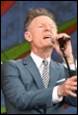 A person in a suit singing into a microphone

Description automatically generated
