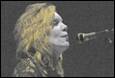 A person with long hair singing into a microphone

Description automatically generated