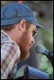 A person with a beard and a hat speaking into a microphone

Description automatically generated