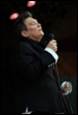 A person in a black suit holding a microphone

Description automatically generated