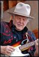 A person in a hat playing a guitar

Description automatically generated