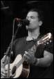 A person singing into a microphone and playing guitar

Description automatically generated