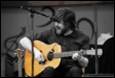 A person playing guitar and singing into a microphone

Description automatically generated