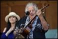 A person playing a guitar with a person behind him

Description automatically generated