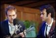 A person playing guitar next to a person holding a microphone

Description automatically generated
