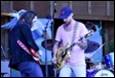 A person playing guitar with a person on stage

Description automatically generated