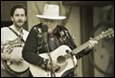 A person playing guitar and a person in a cowboy hat

Description automatically generated