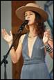A person wearing a hat and dress singing into a microphone

Description automatically generated