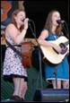 A couple of women singing and playing guitars

Description automatically generated